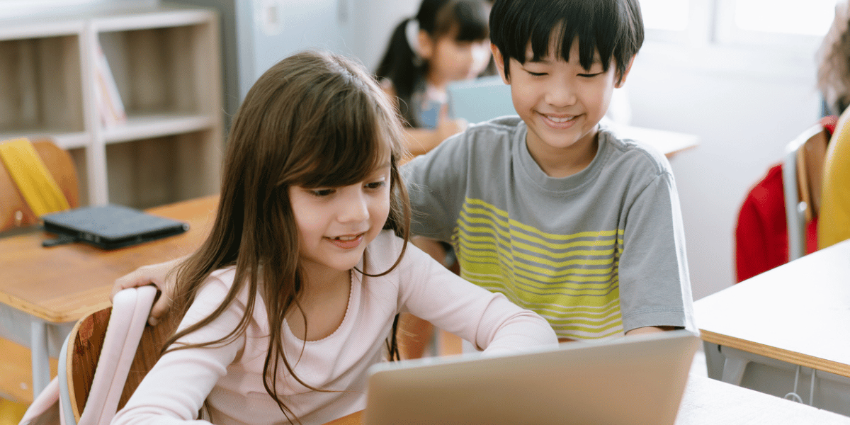 Duas crianças na sala de aula olhando para o notebook e sorrindo.