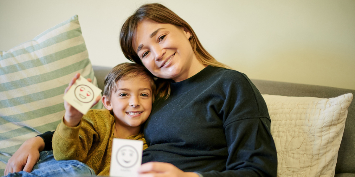 Mãe mostrando para o filho papel com sentimentos para ensinar sobre desenvolvimento da inteligência emocional em casa.