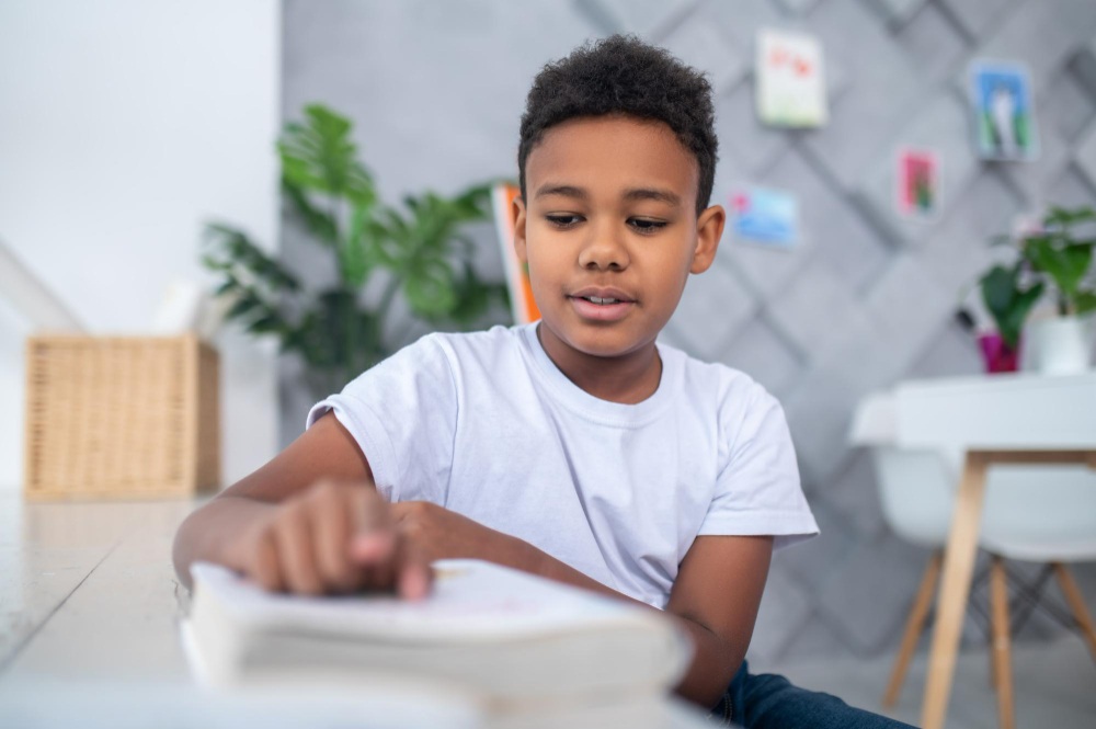 menino lendo cuidadosamente um livro sobre a mesa.