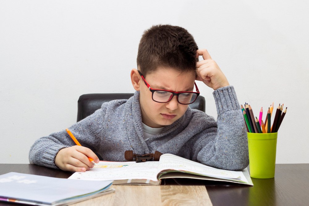 aluno com expressão de frustração enquanto olha para seu livro escolar sobre a mesa.