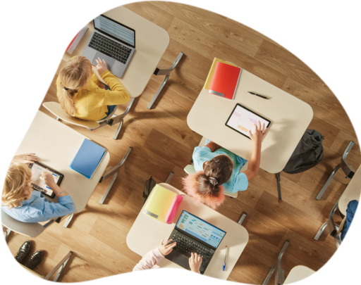 Vista superior da sala de aula no ensino fundamental: crianças sentadas na mesa da escola usando computadores pessoais e tablets digitais para tarefas.