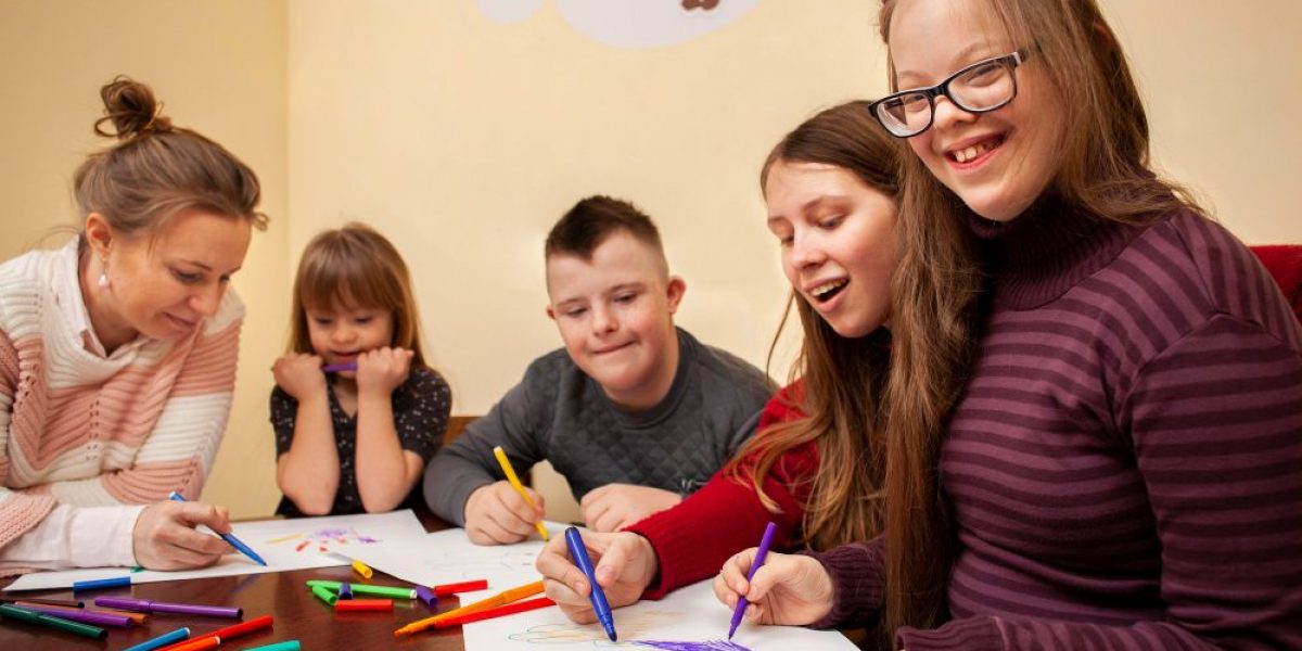 grupo de alunos com necessidades especiais desenham em mesa com orientação de professora